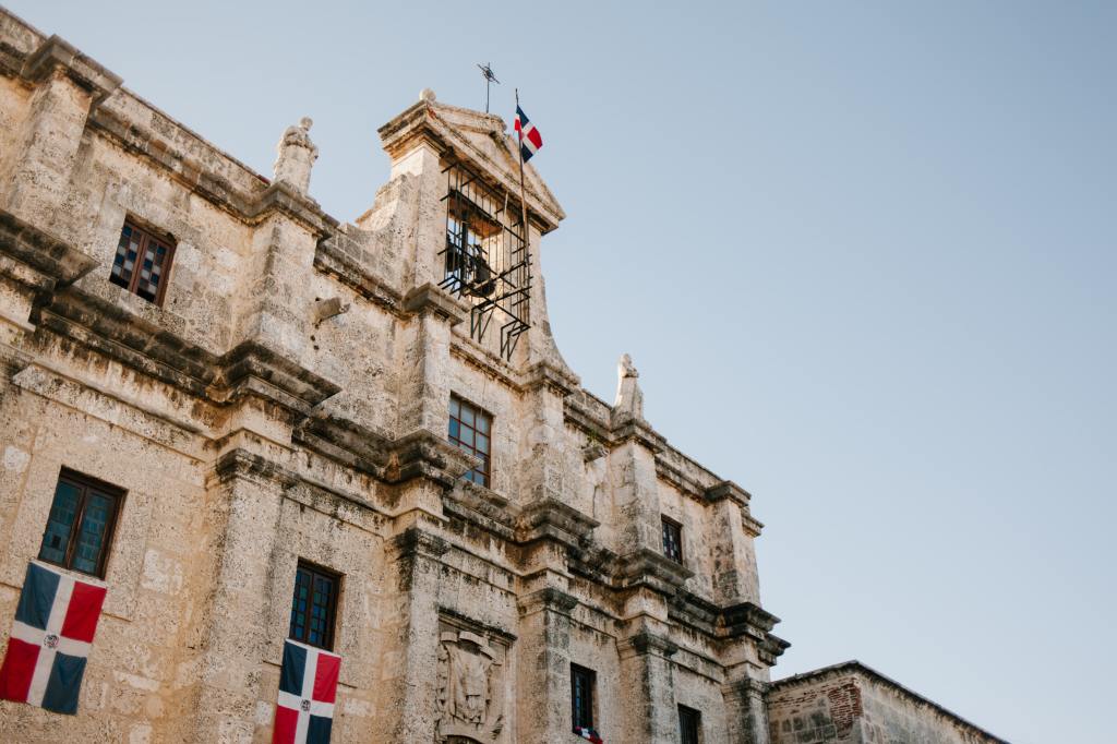 A photo of an old building with Dominican flags hanging from the windows. 